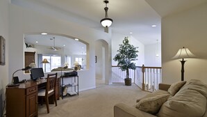 A spacious living room with a large window, a desk with a computer, a comfortable sofa, and a potted plant.