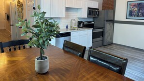 Une cuisine moderne avec des meubles blancs, des appareils en acier inoxydable et un coin repas comprenant une table et des chaises en bois.