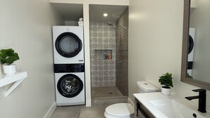 Une petite salle de bain équipée d’un lave-linge, de toilettes et d’une douche.