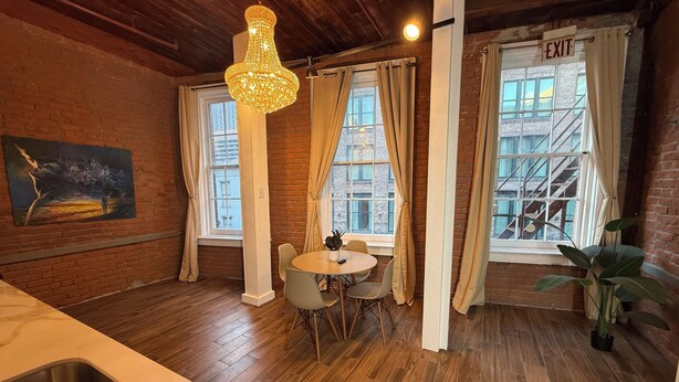 Una habitación acogedora con techo de madera, un candelabro, una mesa de comedor con sillas y ventanas amplias con cortinas.