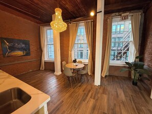 A cozy room with a wooden ceiling, a chandelier, a dining table with chairs, and large windows with curtains.