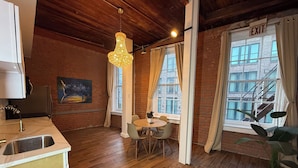 Una habitación acogedora con techo de madera, una mesa de comedor con sillas, una lámpara colgante y vistas a un edificio a través de grandes ventanales.