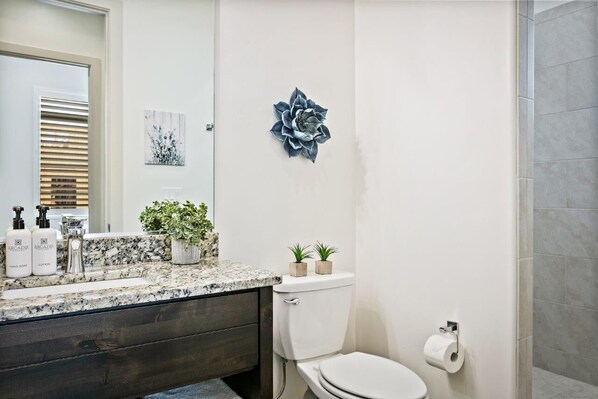 A bathroom with a marble countertop, a toilet, a sink with two plants, and a wall-mounted decorative piece.