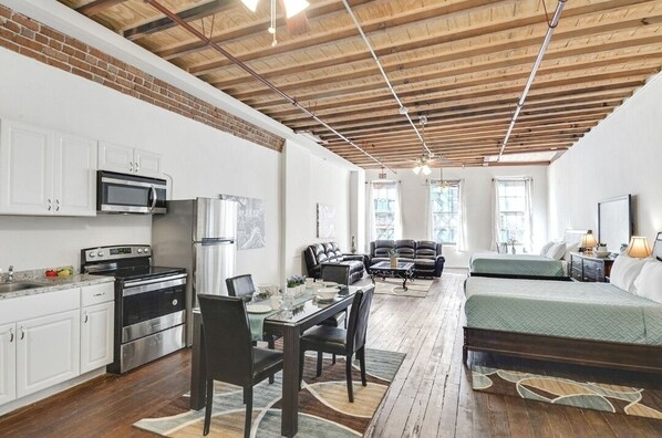Guest room with a kitchenette, dining area, and seating space, featuring a bed and windows with an outside view.