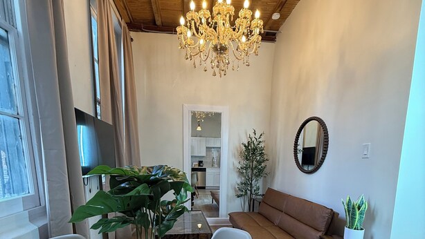 A dining area with a round table, chairs, a chandelier, a potted plant, a sofa, and a mirror.