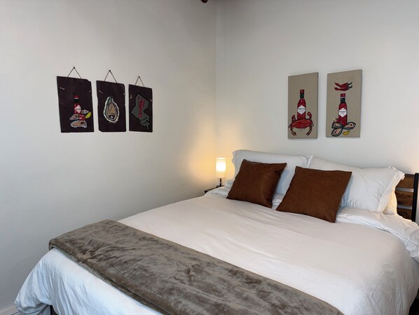 Una cama bien hecha con ropa de cama blanca y marrón, una manta marrón y una mesita de noche con una lámpara.