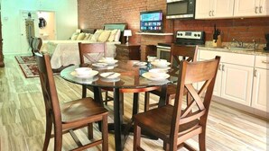 A dining area with a round glass table, wooden chairs, and a brick wall. - Downtown New Orleans Penthouse Suite - 2 Minute Walk to French Quarter -4B (New Orleans)