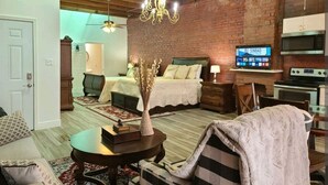 A cozy living room with a fireplace, a bed with a view, and a kitchen area with a TV. - Downtown New Orleans Penthouse Suite - 2 Minute Walk to French Quarter -4B (New Orleans)