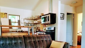 A living room with a sectional sofa, a wooden coffee table, and a kitchen area with appliances and utensils. - Cottage by Lady Bird Lake and Trail (Austin)