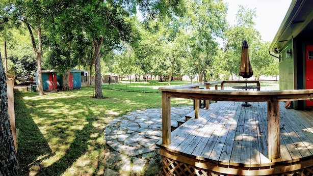 A wooden deck with a stone pathway, a red door, and a green building in the background. - Cottage by Lady Bird Lake and Trail (Austin)