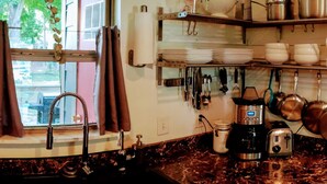 A kitchen with a sink, stove, and various utensils. There are shelves with dishes and a window with curtains. - Cottage by Lady Bird Lake and Trail (Austin)