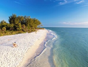 A beach with clear turquoise water, white sand, and dense green foliage.