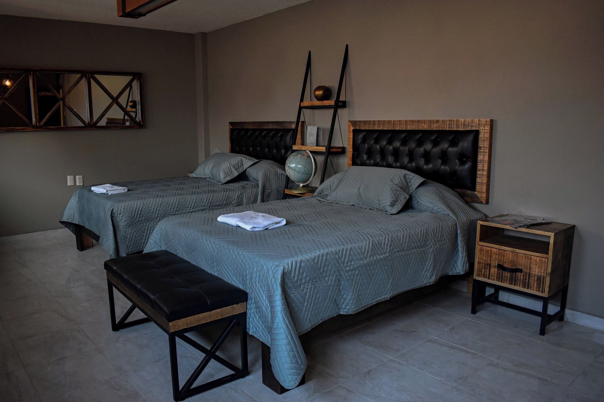 Un dormitorio con dos camas, un banco, una mesita de noche y una estantería en la pared.