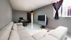 Ett vardagsrum med en soffa, en tv och en matplats med ett bord och stolar.