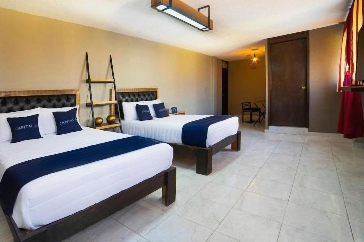 A hotel room with two beds, a wooden headboard, a ladder, and a small table.