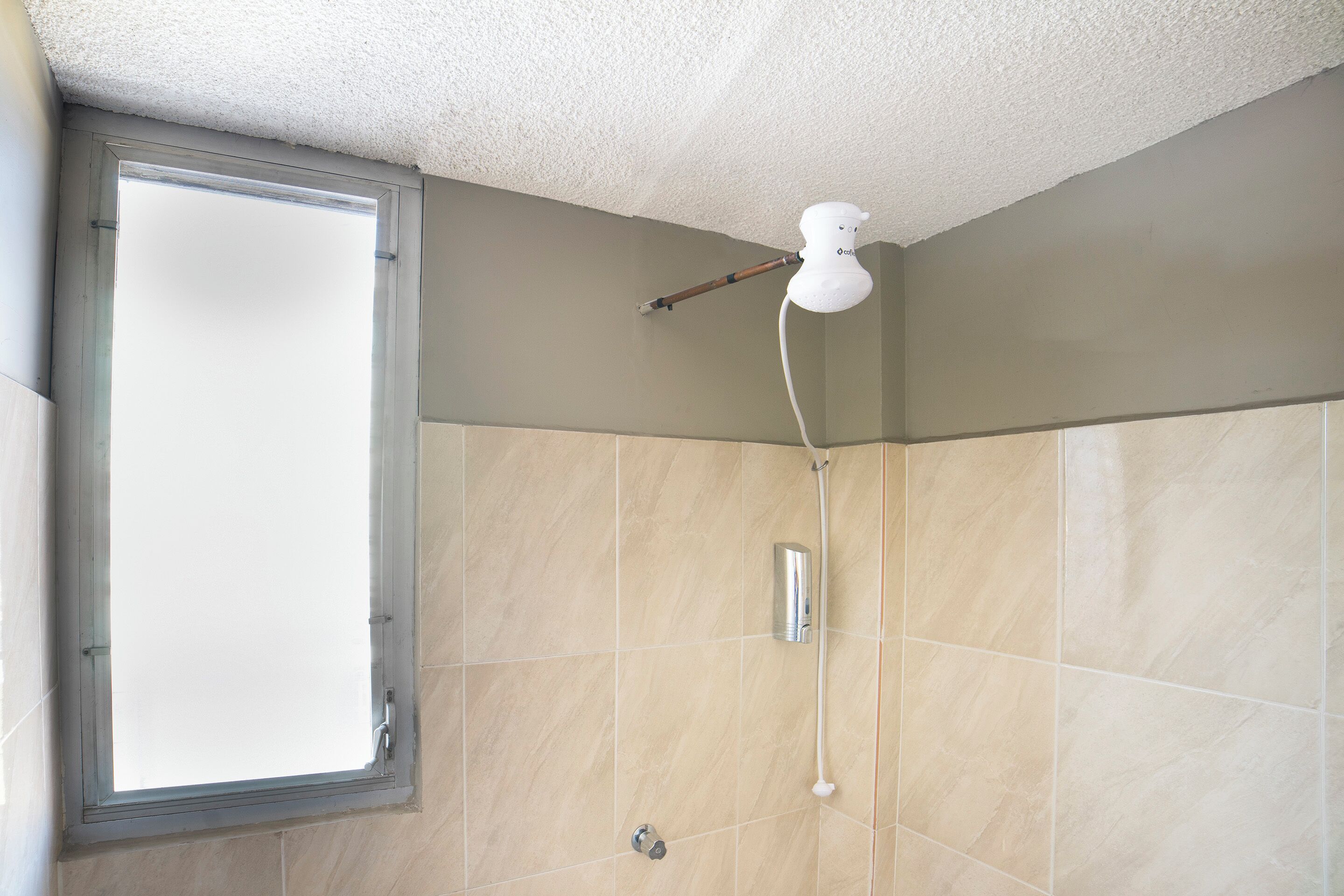 A bathroom with beige tiles, a window, and a showerhead mounted on the wall.