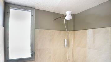 A bathroom with beige tiles, a window, and a showerhead mounted on the wall.