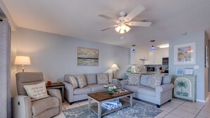 A living room with a sofa, armchair, coffee table, and a ceiling fan. - Beach View - Pelican Cove 3 by SeaBreeze Vacation (Bradenton Beach)