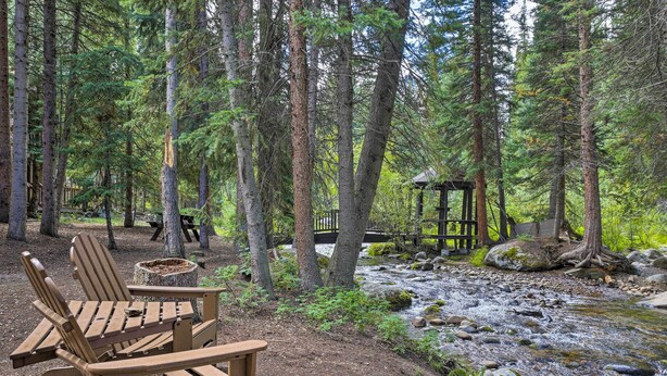 Ein bewaldeter Campingplatz mit Holzsitzen, einem Picknicktisch, einer kleinen Holzhütte und einem Bach.