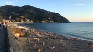 A beach with people sunbathing and swimming, a pier with buildings, and a hillside in the background. - Sant'Antonino Apartments - Scirocco (levanto)