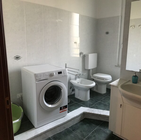 A compact bathroom with a washing machine, toilet, and sink.