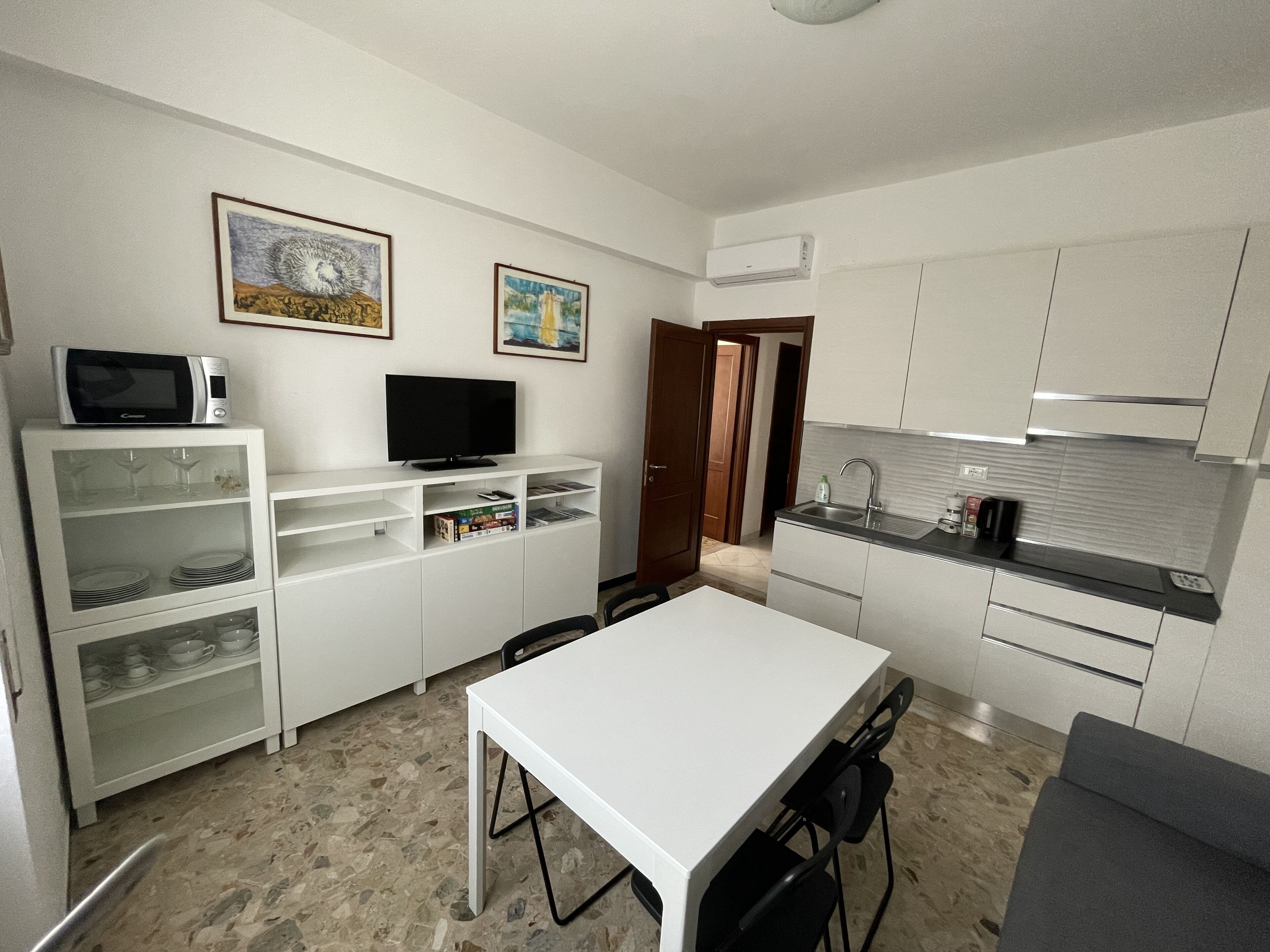 A compact kitchen with white cabinets, a microwave, a flat-screen TV, and a dining area with a table and chairs.