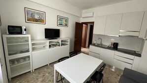 A compact kitchen with white cabinets, a microwave, a flat-screen TV, and a dining area with a table and chairs. - Sant'Antonino Apartments - Scirocco (levanto)
