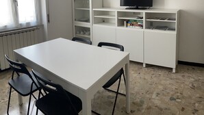 A room with a white table and chairs, a TV on a stand, a cabinet with glass doors, and a window with curtains. - Sant'Antonino Apartments - Scirocco (levanto)