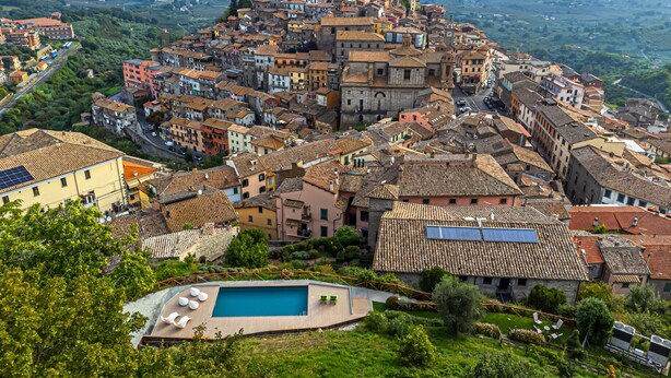 A historic town with a prominent castle on a hill, surrounded by colorful buildings and a swimming pool area.