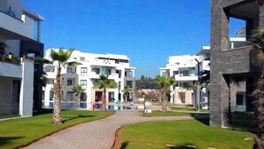 A modern residential complex with a paved walkway, palm trees, and contemporary architecture. - Residence Hivernage Founty 4748 (Agadir)
