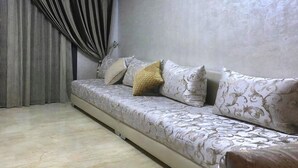 A room with a sofa set against a textured wall, a curtain partially drawn, and a carpeted floor. - Residence Hivernage Founty 4748 (Agadir)