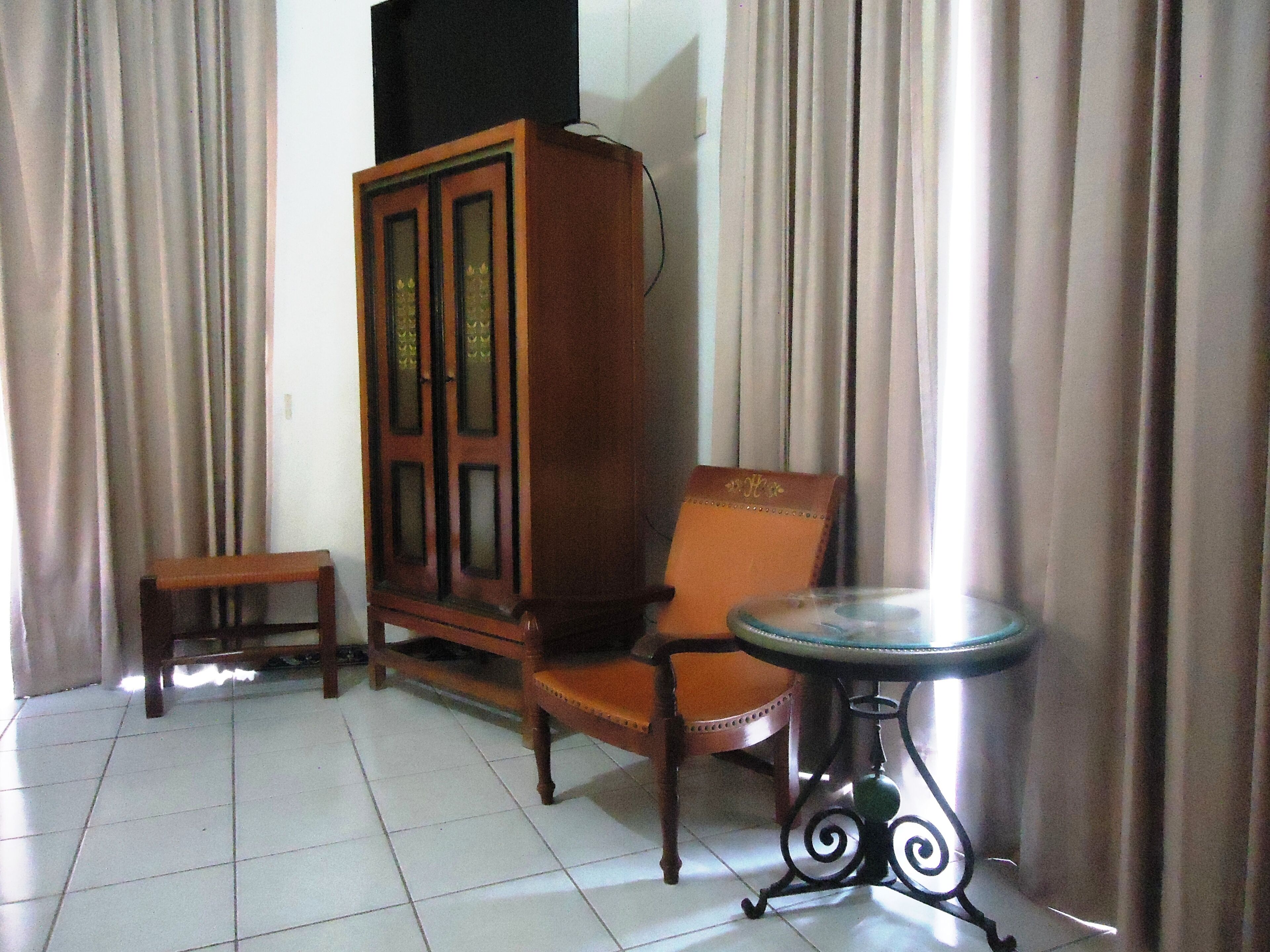 A room with a wooden cabinet, a chair, a small table, and curtains.