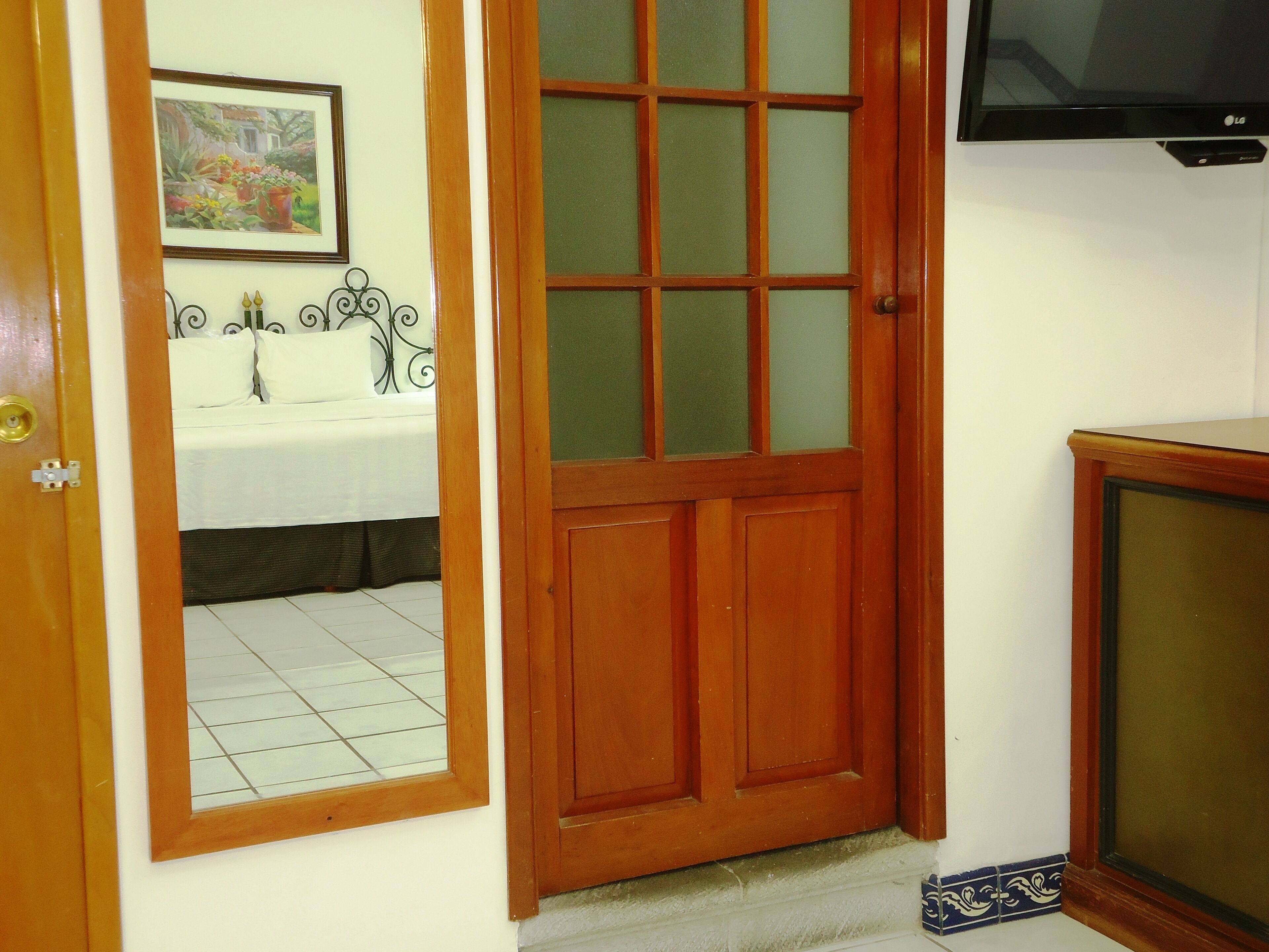 A wooden door with a glass panel, a bathroom with a white sink and a framed picture, and a television mounted on the wall.