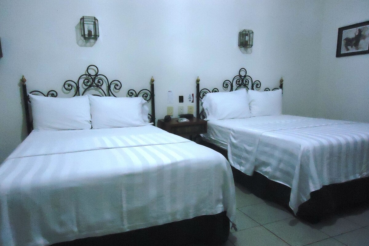 Dos camas individuales con cabeceros metálicos, ropa de cama blanca y suelo de baldosas.