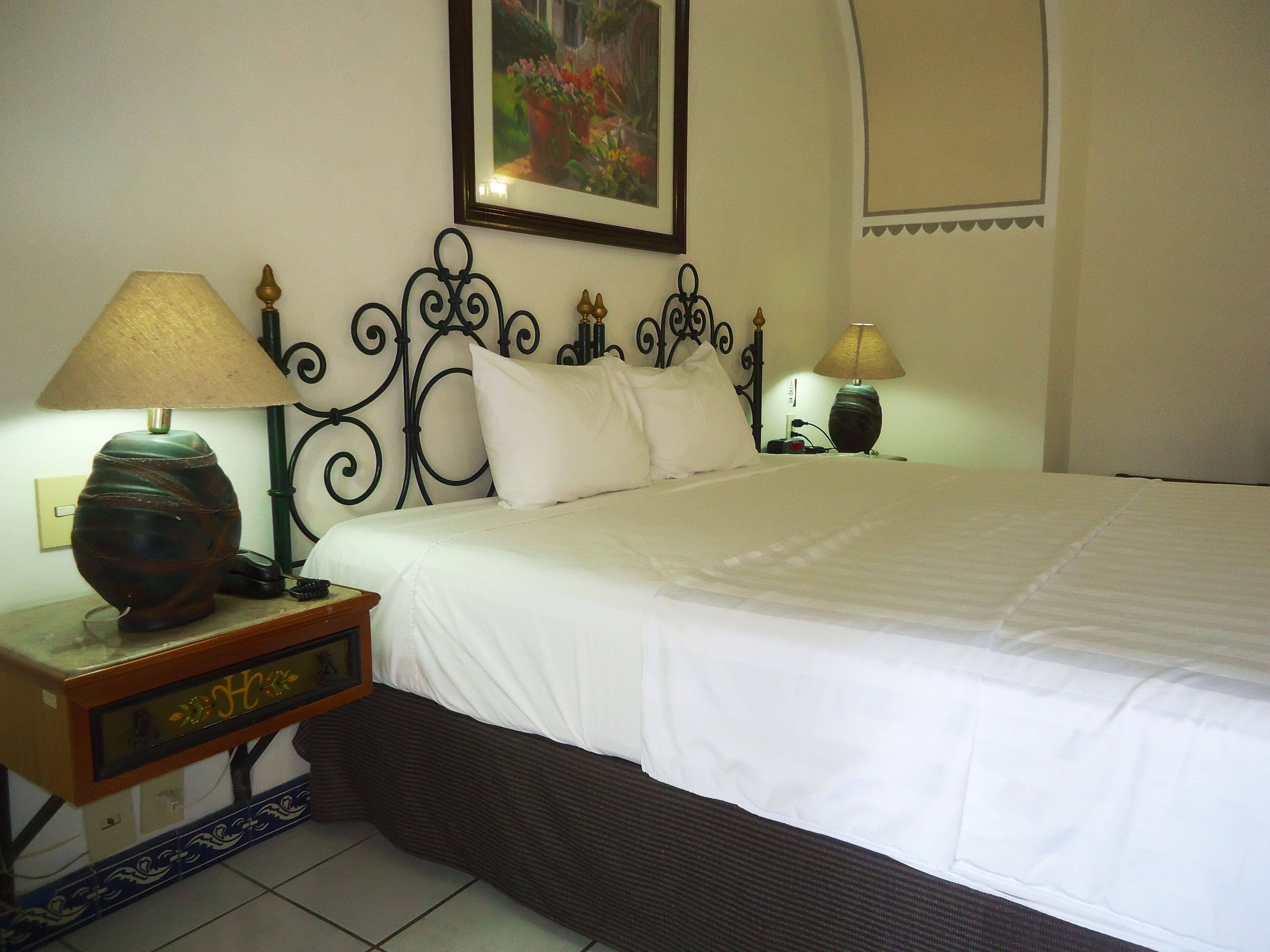 A neatly made bed with white linens, two bedside lamps, a decorative wall piece, and a small table with a lamp and a decorative item.