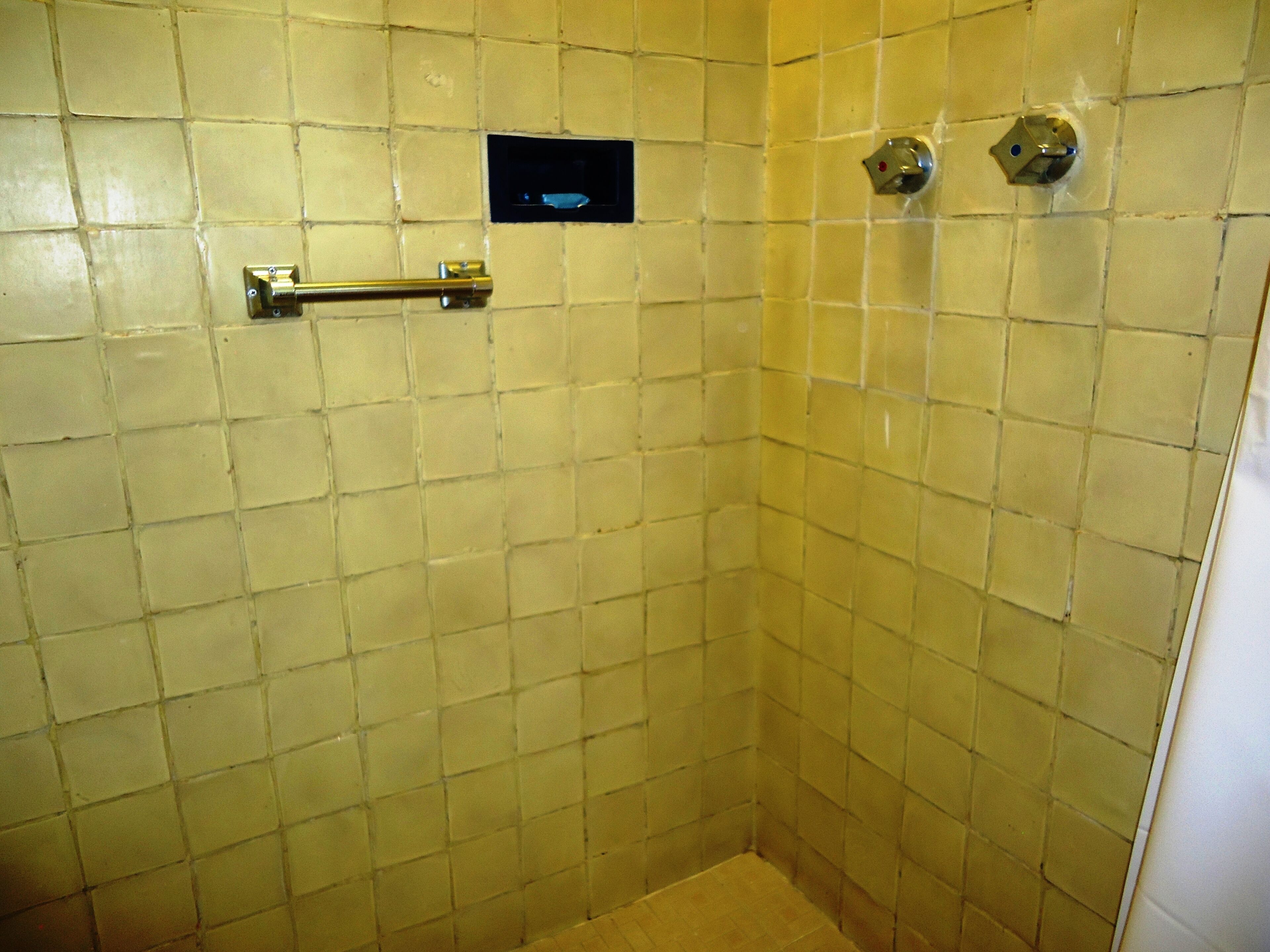 Un box de ducha con azulejos, un pasamanos y un panel de control.