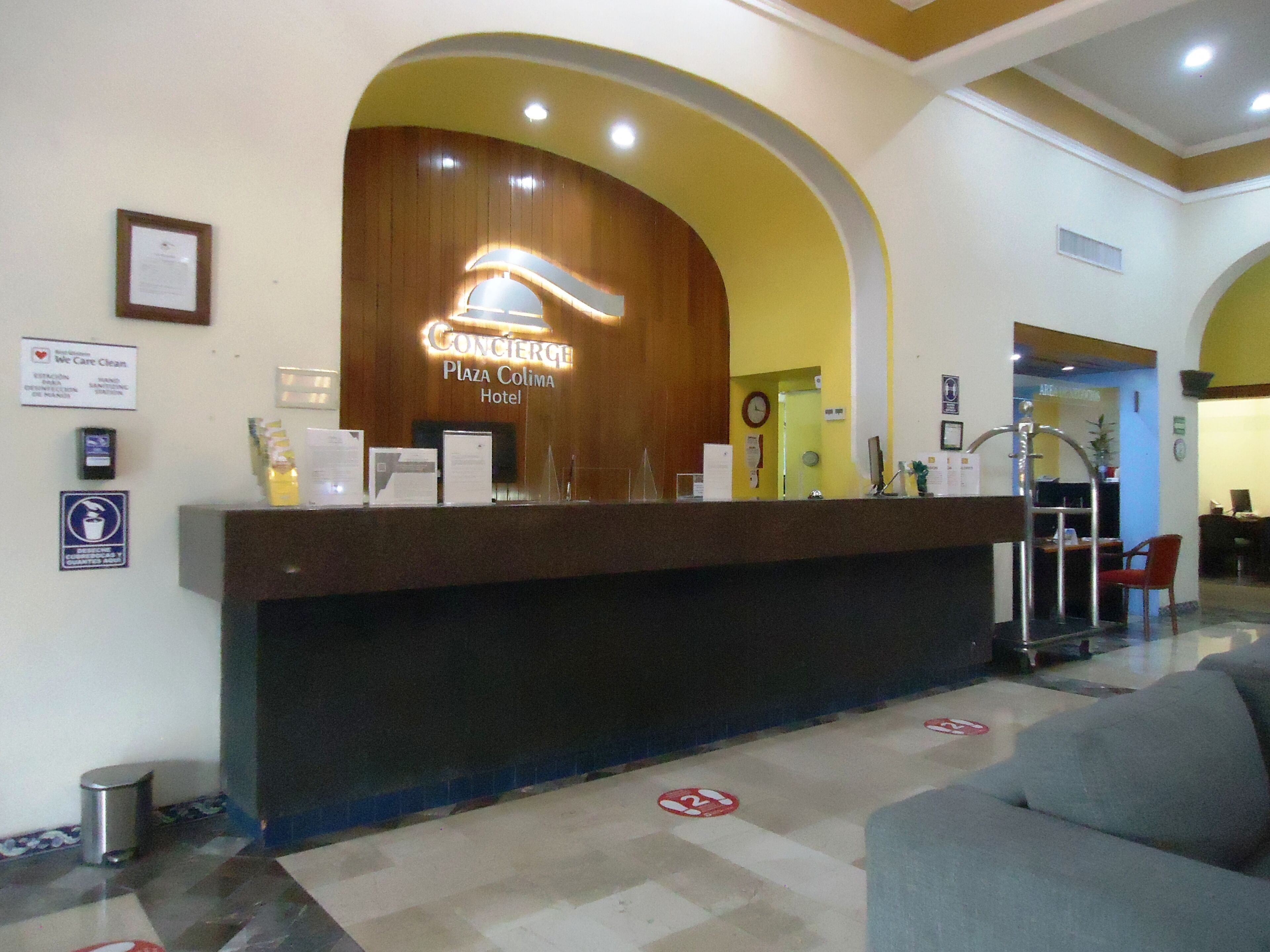 A hotel reception desk with a wooden backdrop and a sign reading "Concierge Plaza Colima Hotel".