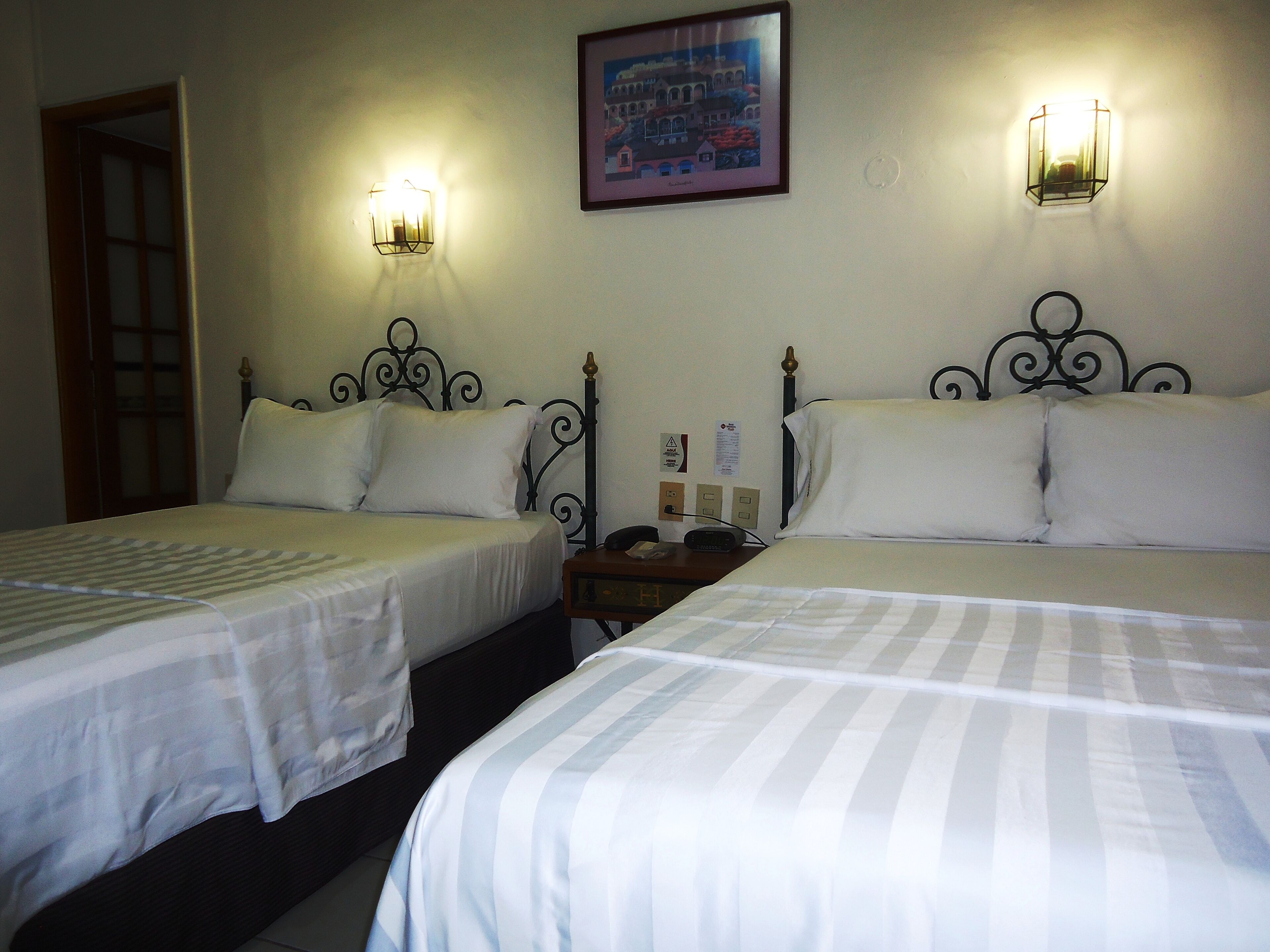 Habitación de hotel con dos camas, cada una con ropa blanca y un estampado a rayas. Hay lámparas de pared a ambos lados de las camas.