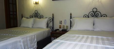 Habitación de hotel con dos camas, cada una con ropa blanca y un estampado a rayas. Hay lámparas de pared a ambos lados de las camas.