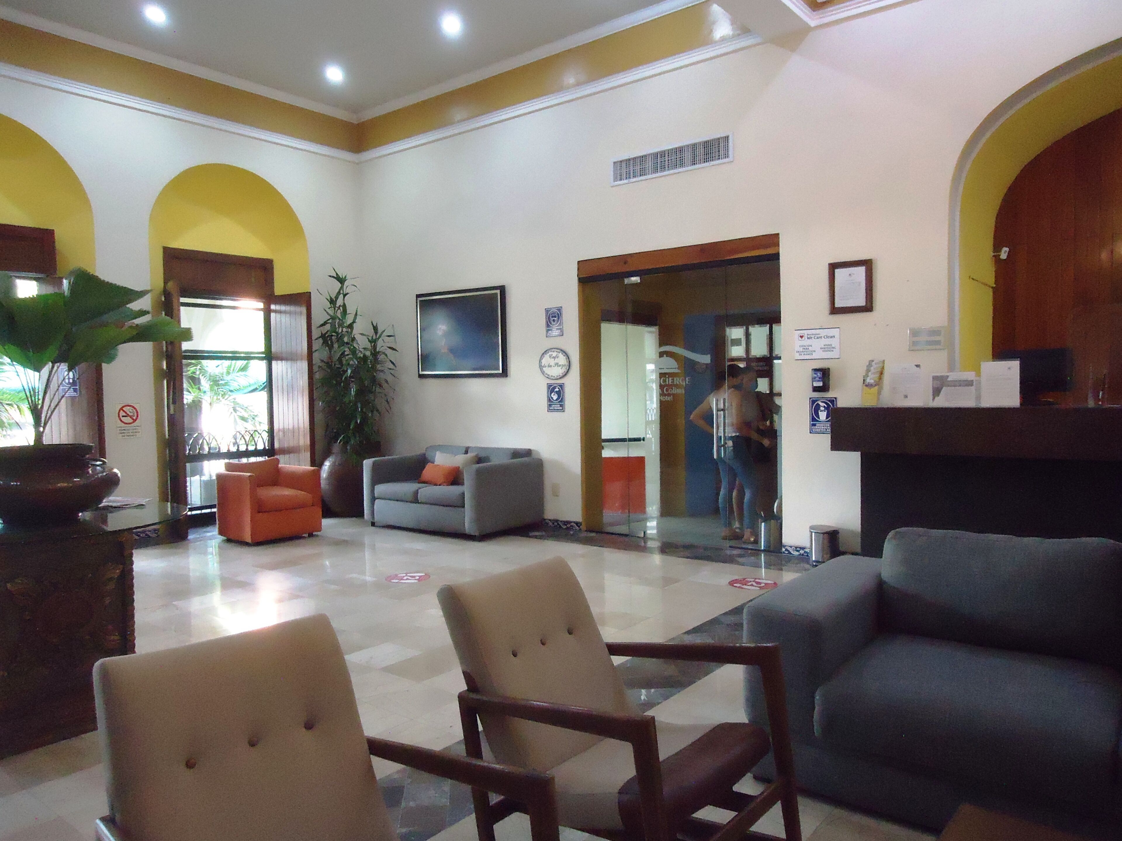 A hotel lobby with a reception desk, seating area, and a large plant.