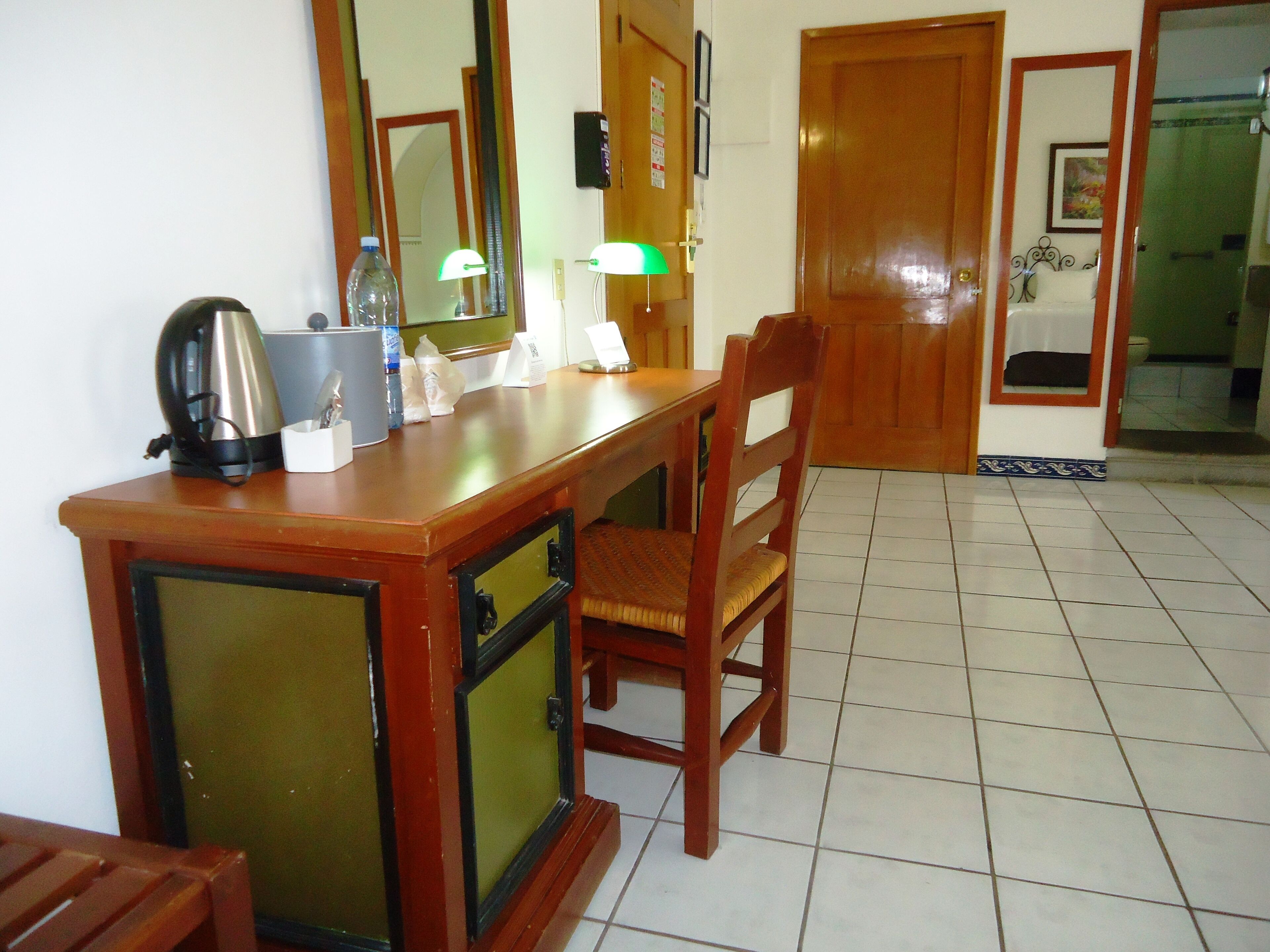 A wooden desk with a kettle, a bottle, and a lamp in a room with tiled flooring and wooden doors.