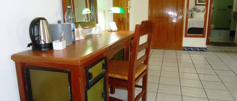 A wooden desk with a kettle, a bottle, and a lamp in a room with tiled flooring and wooden doors.