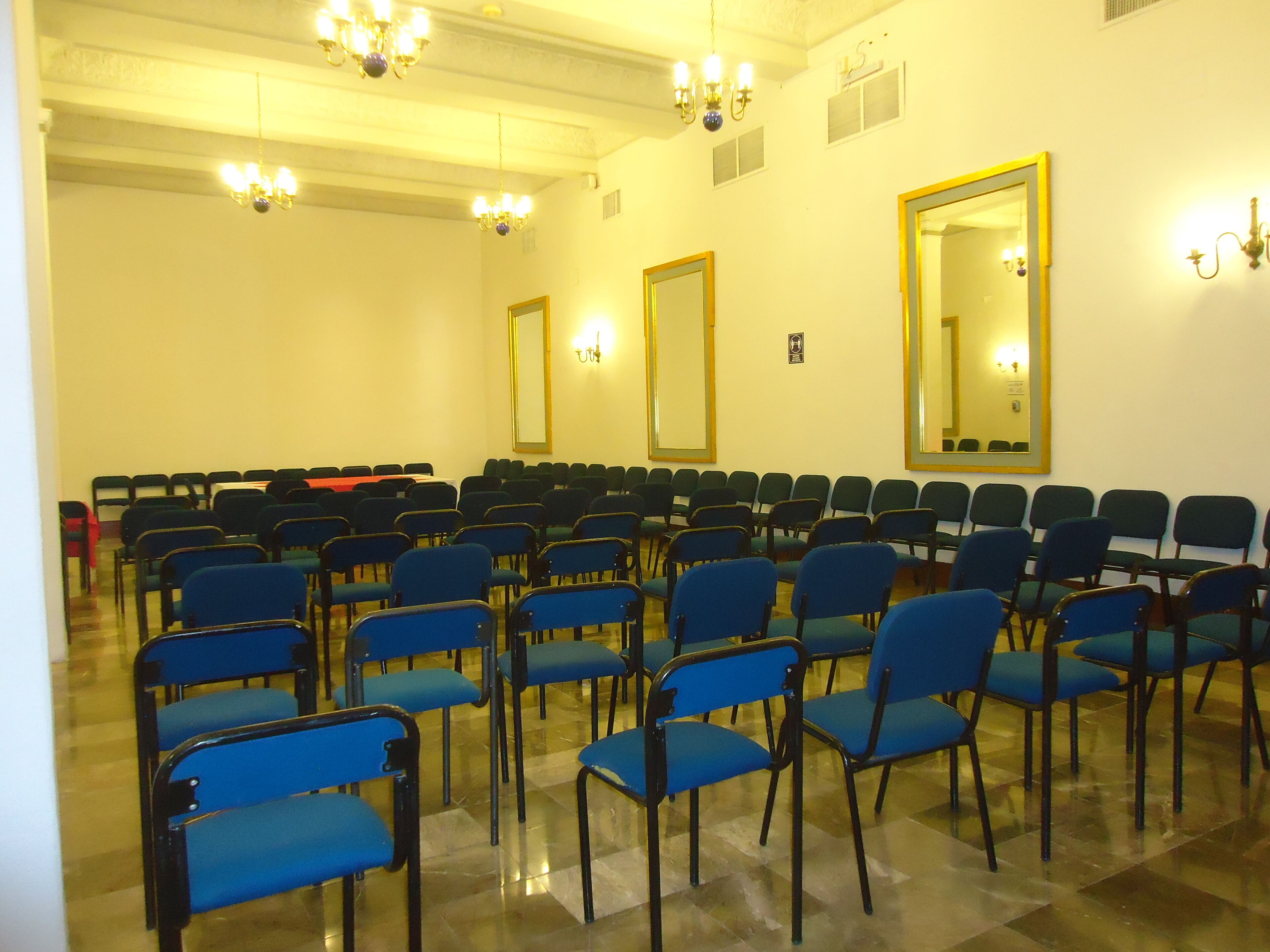 A conference room with rows of blue chairs, a large mirror, and chandeliers.