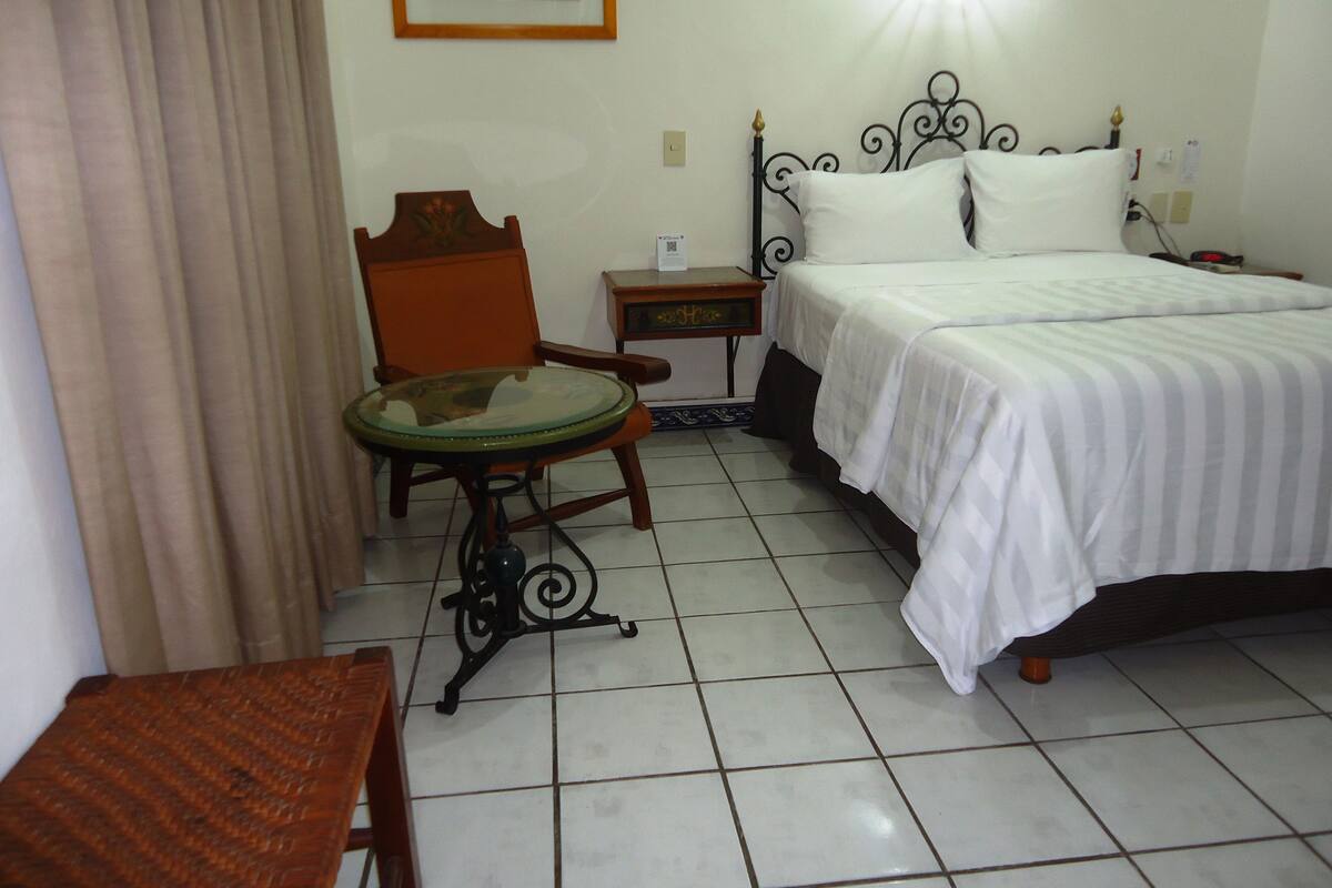 A hotel room with a bed, a chair, a small table, and a nightstand.