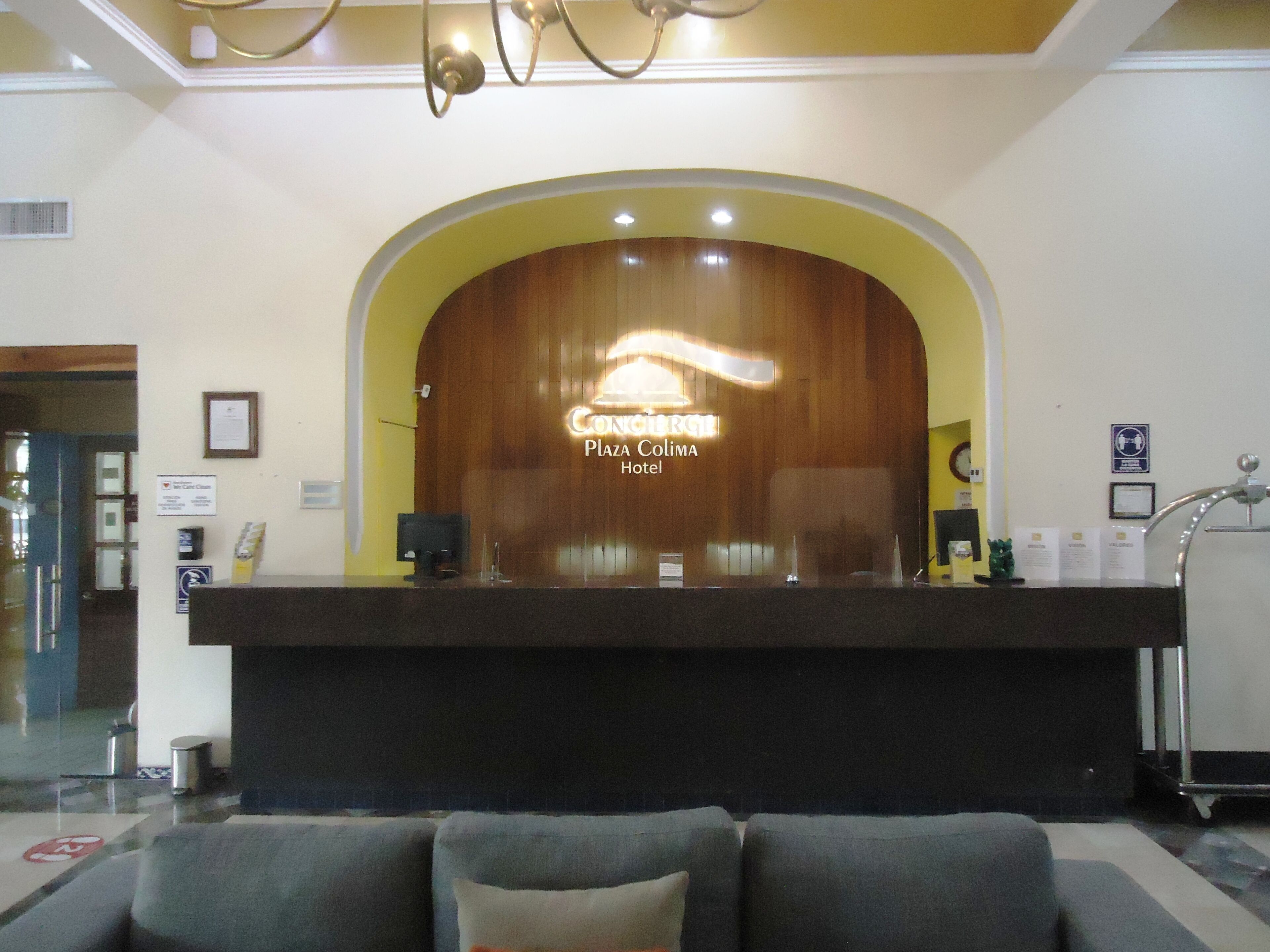 A hotel reception desk with a sign reading "Coniglio Plaza Colima Hotel".