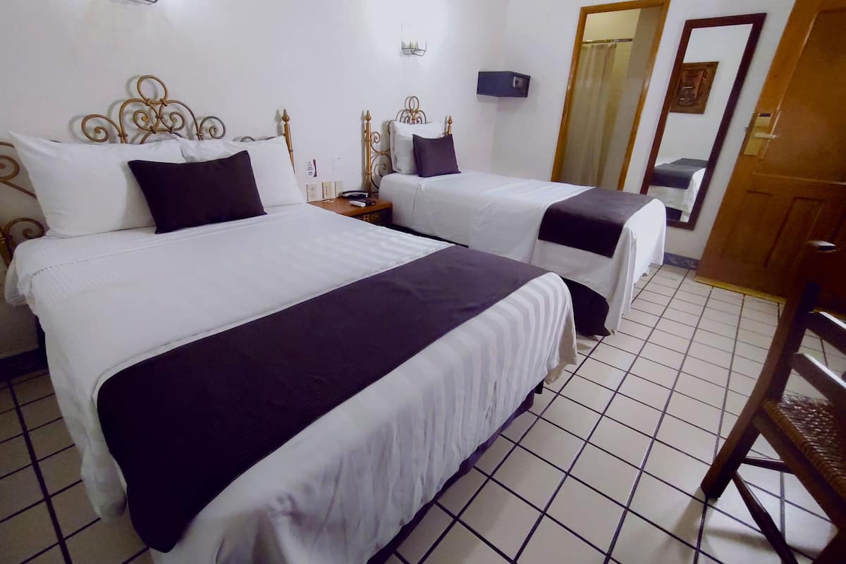 A hotel room with two beds, each with a white and dark-colored bedspread, a wooden nightstand, a wall-mounted lamp, and a mirror.