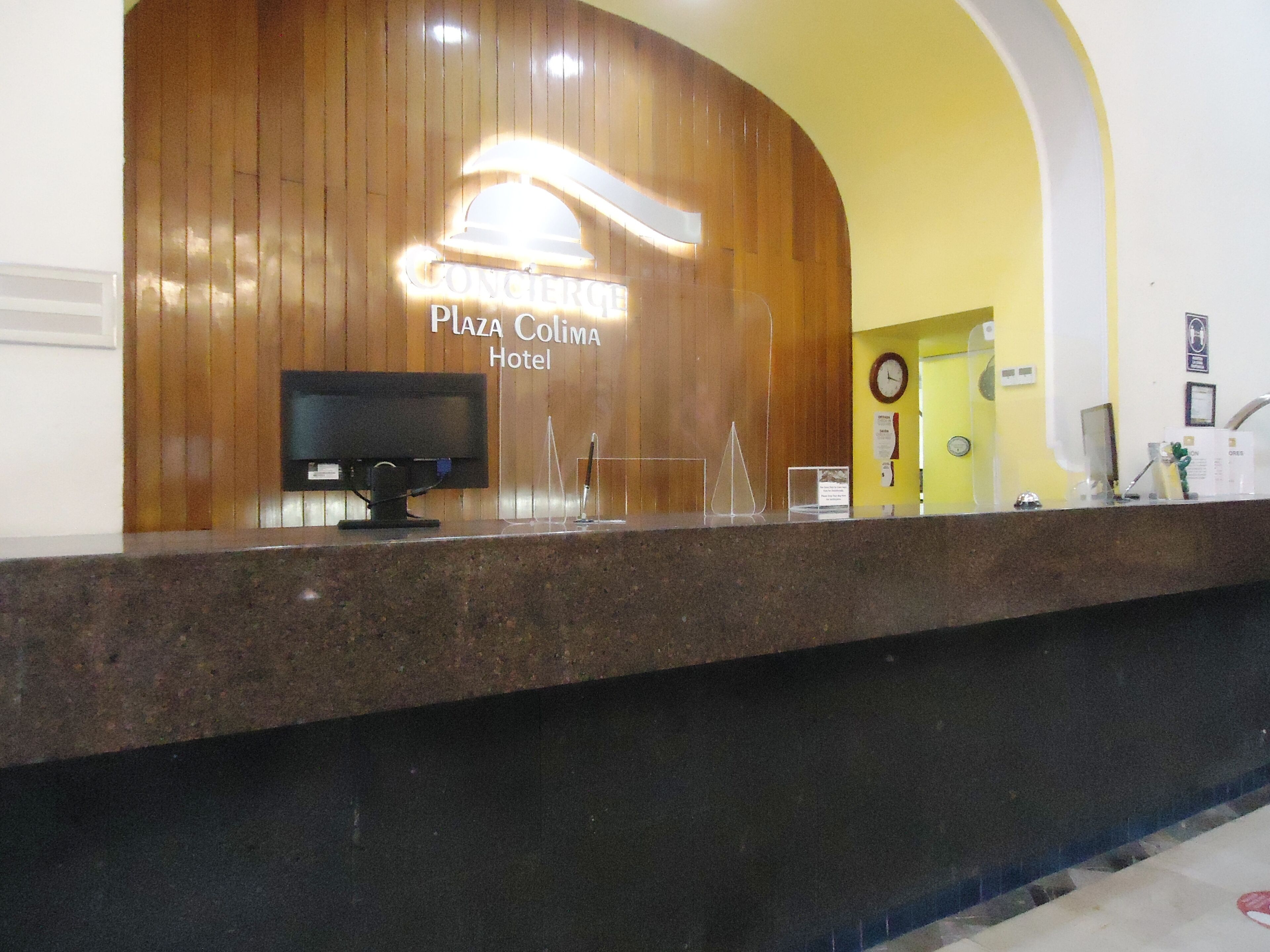Ein Hotelrezeptionstresen mit Holzpaneelen im Hintergrund, einer Uhr und einem Computermonitor.