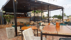 Un café en plein air avec des tables et des chaises en bois, un espace de repos couvert et une enseigne sur laquelle on peut lire : « NOS GUSTA DE SER DE AQUI ».