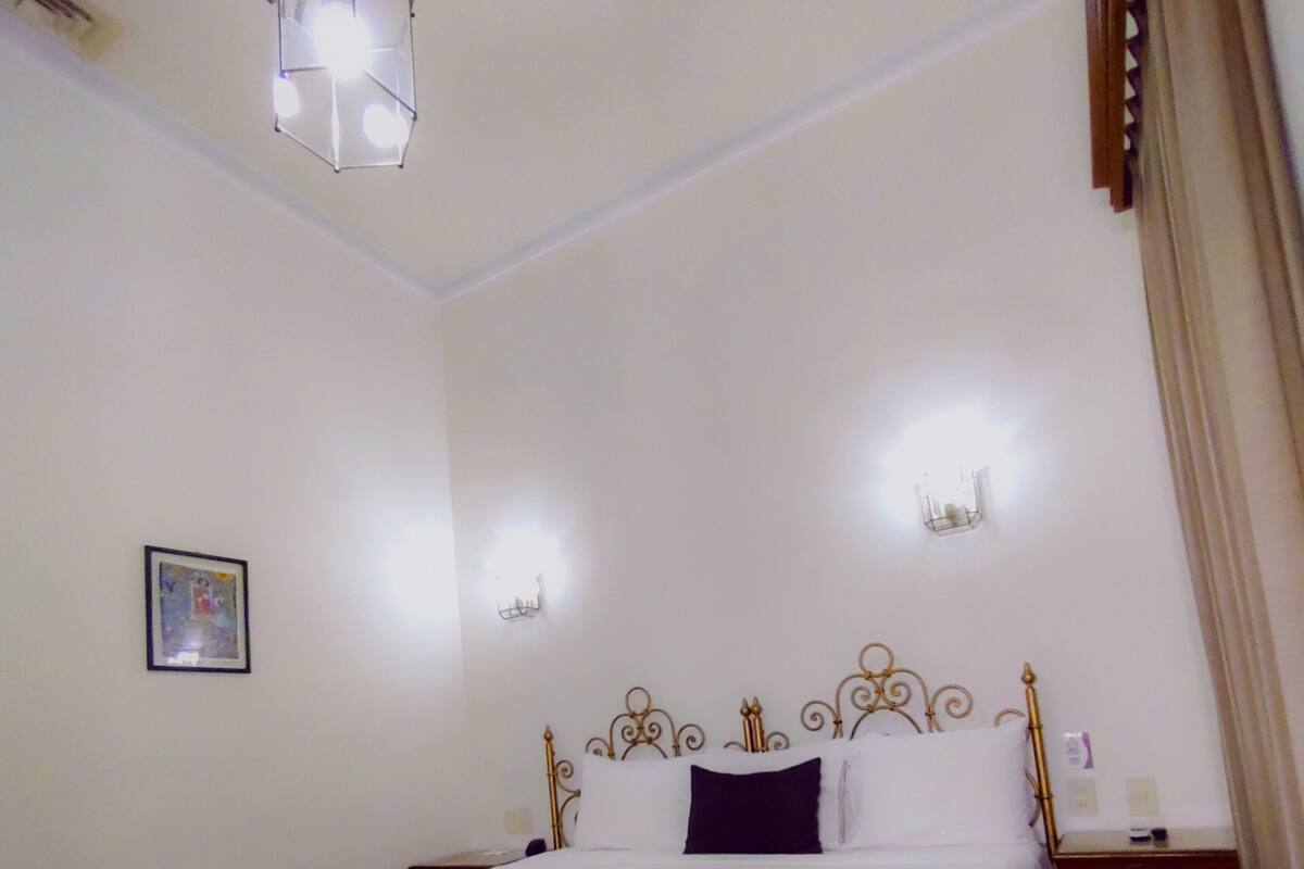 A neatly made bed with a white and dark-colored bedspread, a metal headboard, and a hanging light fixture above.