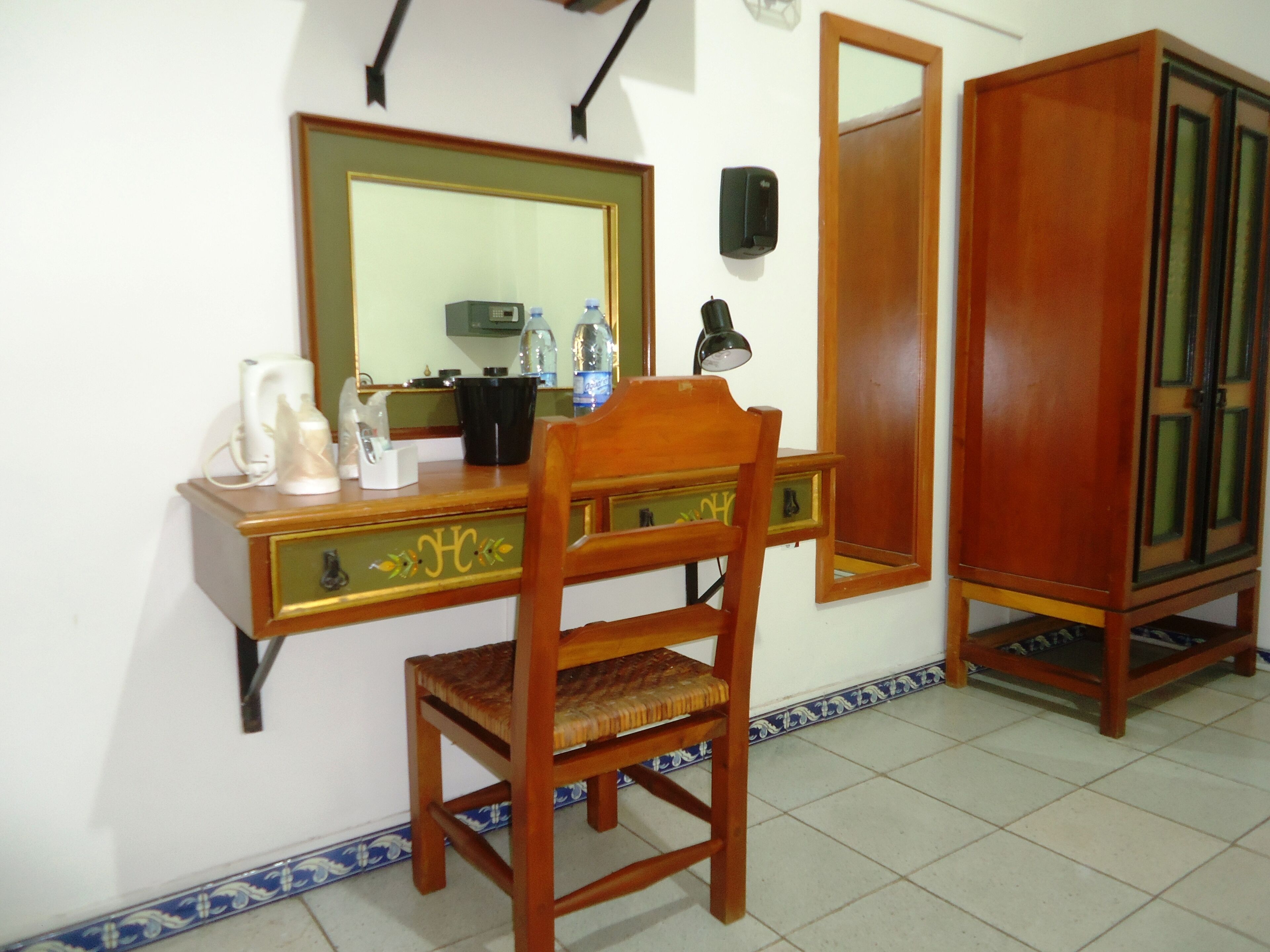 Un escritorio de madera con un espejo, una silla, un teléfono y un mueble bajo.